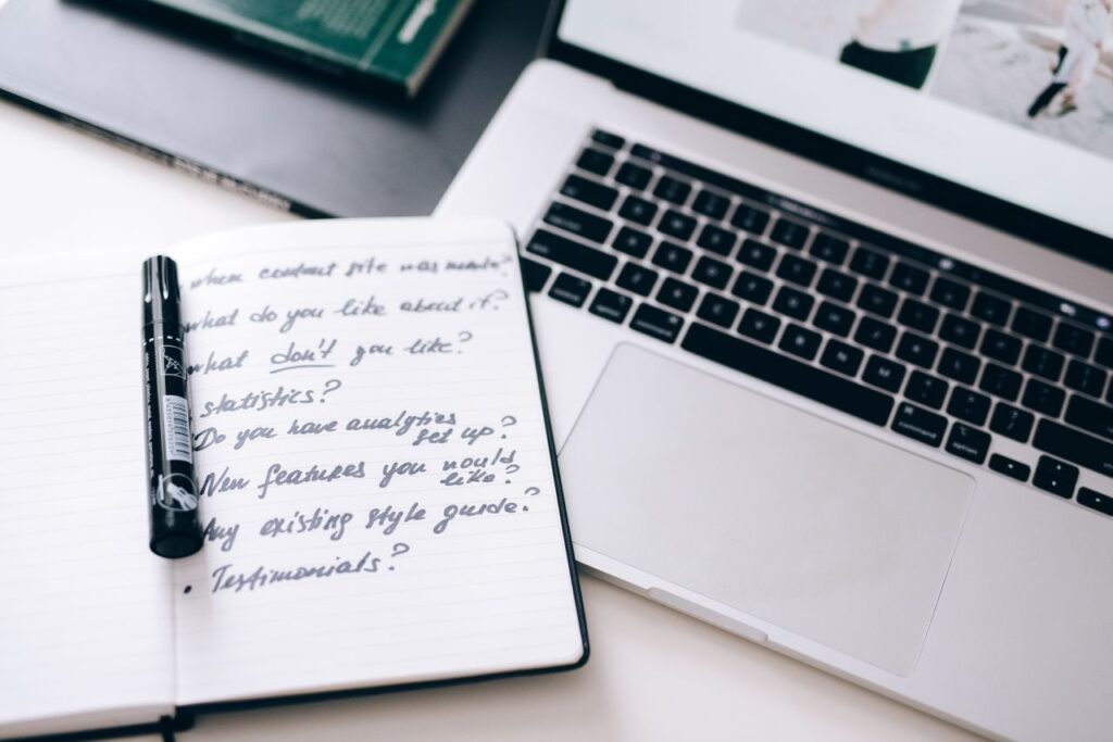 A notebook with handwritten notes next to a laptop on a workspace desk.